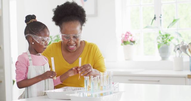 Grandmother and granddaughter wearing safety goggles conducting a science experiment at home kitchen. Both are holding test tubes, indicating hands-on participation and learning. This can be used for showcasing family bonding over educational activities, promoting STEM education, or advertising educational products and services.
