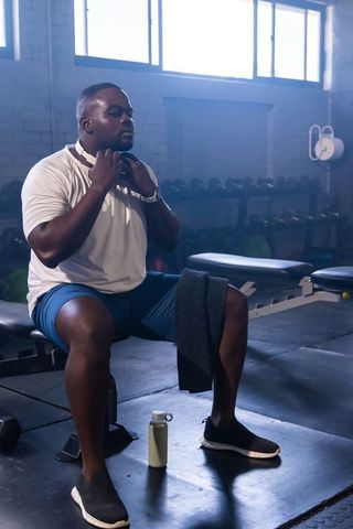 Male athlete resting on bench in gym adjusting shirt, towel on thigh, water bottle nearby