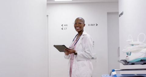 Confident clinician in lab coat holding tablet in sterile hospital imaging corridor