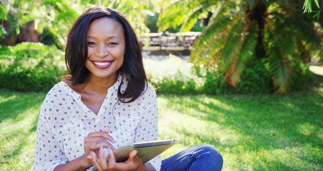 Young woman using tablet while sitting on grass in sunny park - Download Free Stock Images Pikwizard.com