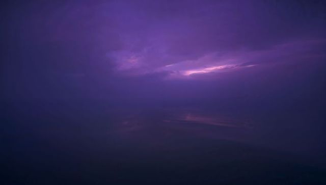 Violet Dawn Over Calm Sea with Glowing Cloud Break, Faint Reflection and Misty Horizon