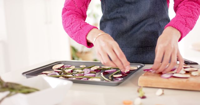 This image depicts a woman arranging sliced vegetables on a tray in a modern kitchen. This can be used for themes related to healthy eating, home cooking, food preparation, and lifestyle blogging. It is ideal for culinary articles, home recipe books, meal planning segments, and social media shares focused on cooking or healthy living.