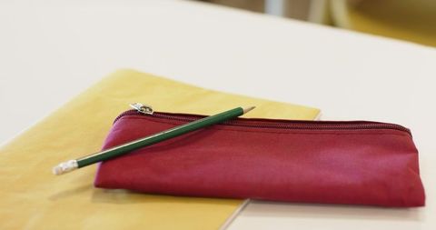 Maroon pencil pouch resting on yellow folder with green pencil on white desk