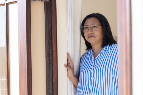 Mature asian woman standing at doorway looking out, contemplative sunlit interior portrait