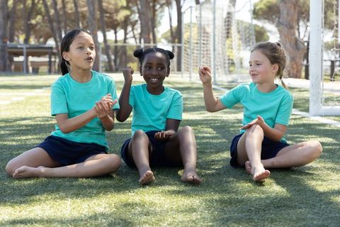 Multiracial schoolgirls clapping and chanting on soccer field in matching teal shirts