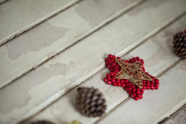 This image shows a close-up of a rustic star decoration made from red beads and twine, placed on weathered wooden planks. Pine cones are scattered around, adding to the festive and natural feel. Ideal for use in holiday-themed projects, DIY craft inspiration, or seasonal marketing materials.