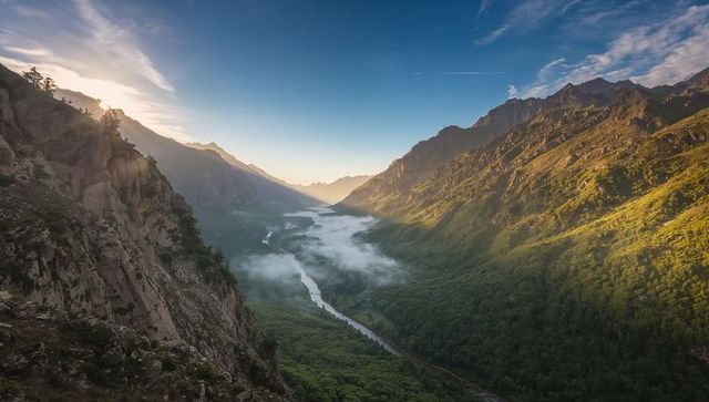 Golden sunrise over alpine valley with meandering river, low mist and rugged cliffs