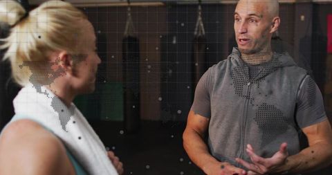 Male trainer explaining boxing technique to female client one-on-one in gym with towel and bags