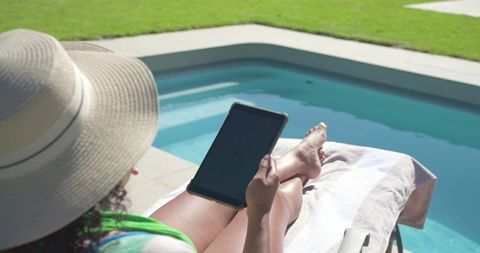 Relaxing by pool holding tablet and wearing sun hat, summer leisure and outdoor relaxation