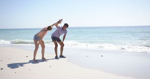 Couple Stretching on Sandy Beach with Ocean Backdrop
