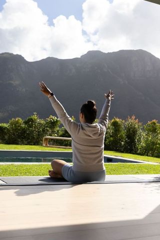 Practicing morning yoga on patio overlooking mountain range and pool, stretching to sky