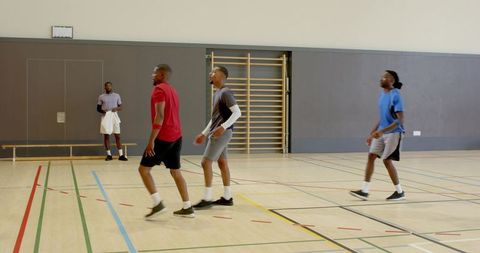 Five men jogging across indoor gym court during team training session near climbing frame