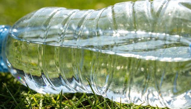 Sunlit plastic water bottle lying on grass showing ripples and prism reflections
