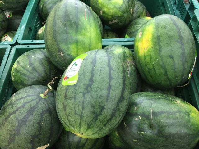Fresh watermelons on display and stacked in green plastic crates at a market. Perfect for use in grocery store ads, healthy eating campaigns, farmers market promotions, and summer food blogs.
