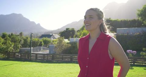 Smiling woman standing on sunlit lawn with mountain garden backdrop