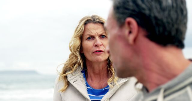 Mature couple arguing near the ocean with emotional intensity, highlighting relationship struggles. Man and woman express stress and anger, suitable for use in articles about relationship difficulties, emotional conflict, or depicting scenes of everyday marital issues.