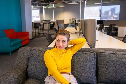 Young woman sitting on gray sofa in modern coworking lounge wearing yellow turtleneck