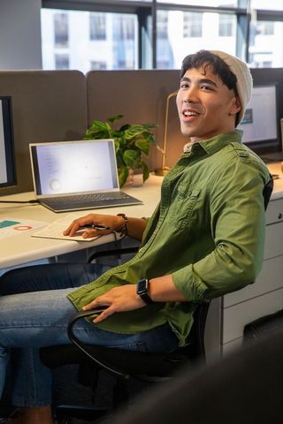Young asian man smiling while working at open plan office desk with laptop analytics dashboard