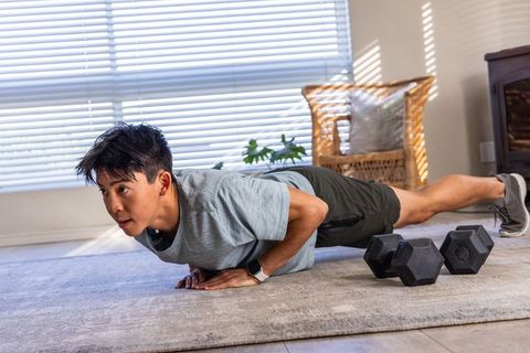Asian man performing push-up at home with dumbbells for home workout and strength training