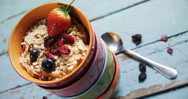 A colorful stack of bowls filled with crunchy cereal topped with fresh strawberries, blueberries, and dried cranberries, on a rustic wooden table. Ideal for health and wellness blogs, breakfast marketing, menus, diet and nutrition campaigns.