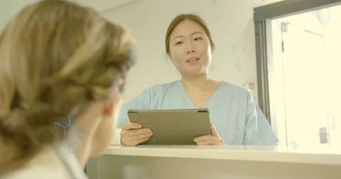 Korean nurse holding tablet and speaking with patient at bright clinic counter