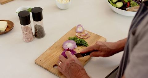 Senior Woman Slicing Red Onion on Wooden Board in Kitchen