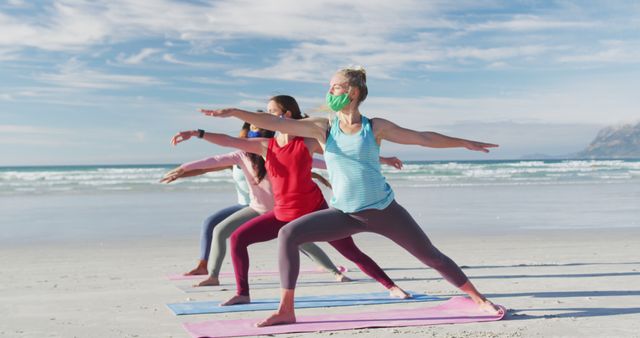 Women practicing yoga on beach wearing masks for health and safety. Suitable for promoting healthy lifestyle, outdoor fitness activities, and pandemic-related safety measures. Ideal for websites and articles related to holistic wellness, stress relief, and outdoor community activities.