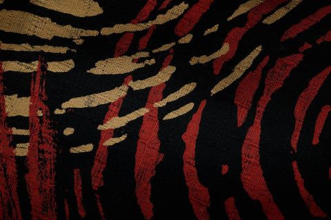 Textured black fabric with abstract red and gold brushstroke animal print pattern