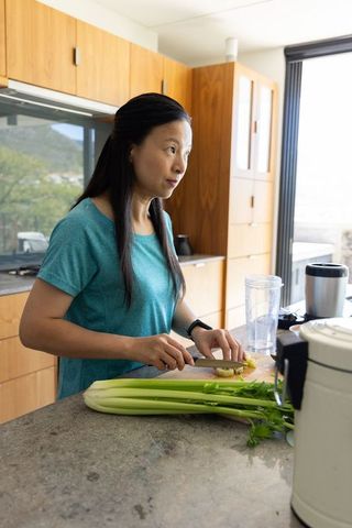Mature asian woman slicing ginger in modern sunlit kitchen preparing healthy meal