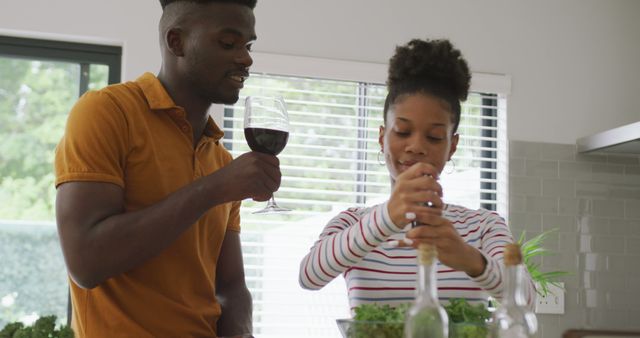 Image of happy african american couple cooking together in kitchen with wine. love, relationship, togetherness and spending quality time at home.