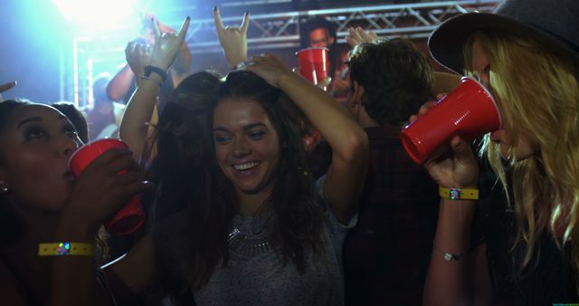 Young adults are enjoying a vibrant party atmosphere, with some holding red cups and dancing under colorful lights. The scene captures the energy and excitement of nightlife entertainment.