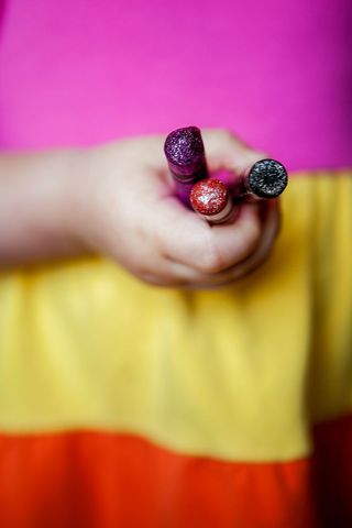 Child holding glitter crayons showcasing purple red black tips over color block dress