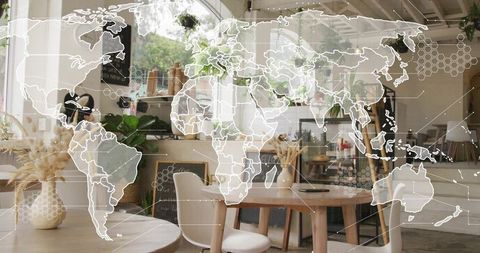 Sunlit cozy cafe workspace featuring world map overlay on wooden table with laptop and pampas vase
