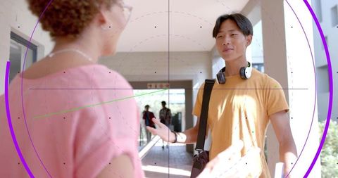 College student greeting peer in sunlit campus corridor holding binder and headphones