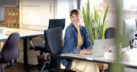 Smiling woman working on laptop in modern open-plan office