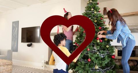 Friends decorating christmas tree with baubles and tinsel in livingroom wearing headbands