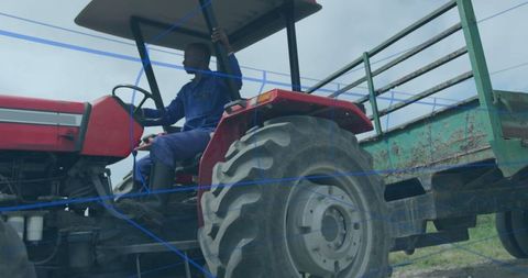 Farmer driving red tractor with green trailer in rural field setting