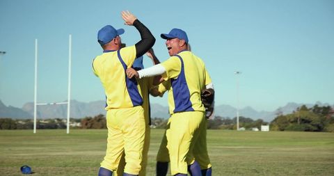 Three teammates celebrating on field in yellow and blue uniforms