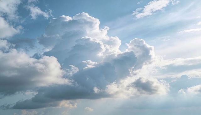 Sunlit Billowy Cumulus Clouds Casting Crepuscular Rays Over Expansive Blue Sky