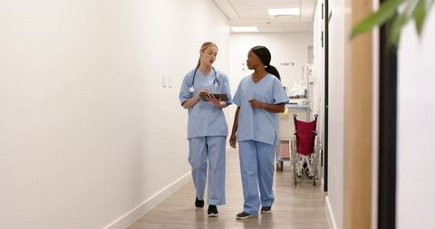 Two nurses walking and reviewing patient notes on tablet in hospital corridor