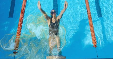 Female Swimmer Launching Off Start Block Pushing Into Backstroke in Sunlit Pool
