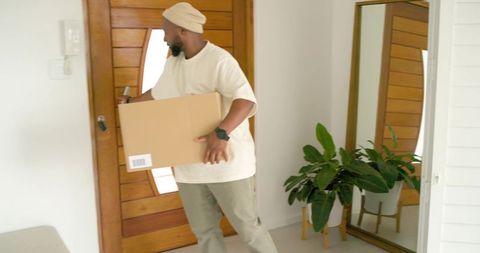 Delivery worker entering modern home carrying cardboard box while unlocking door in minimalist foyer