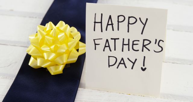 A festive yellow bow adorns a dark blue gift with a handwritten Happy Father's Day! note, with copy space. Such images evoke the celebration of fatherhood and the appreciation for fathers worldwide.