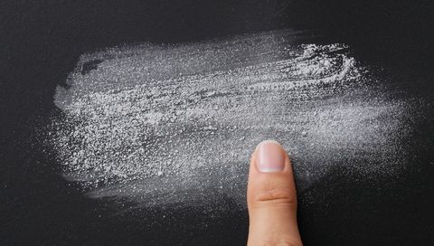 Single fingertip smearing white chalk streak across dark chalkboard with powder texture