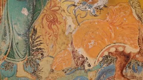 Handheld video revealing weathered temple mural with green-robed figure and orange blossom