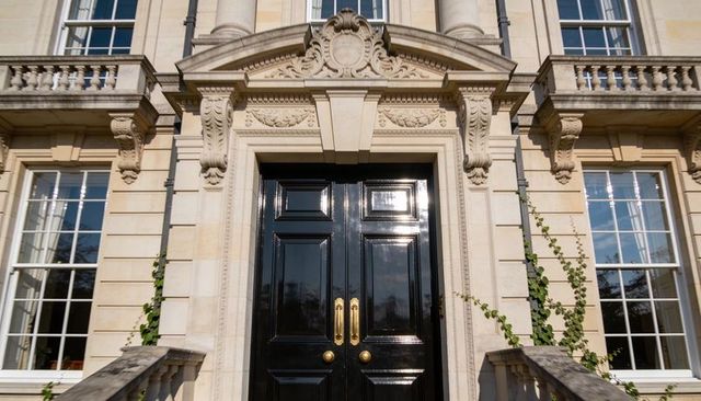 Glossy black double door with brass handles at georgian neoclassical stone entrance