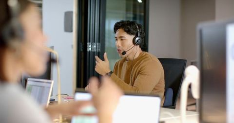 Male coworker speaking and gesturing with headset during team call in modern office