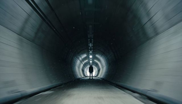 Solitary silhouette walking toward light in moody curved concrete tunnel