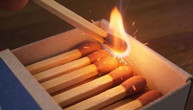 Striking wooden match igniting bright flame with flying sparks macro closeup
