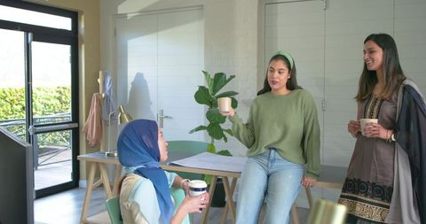Diverse women collaborating over coffee in coworking space with headscarf and green knit